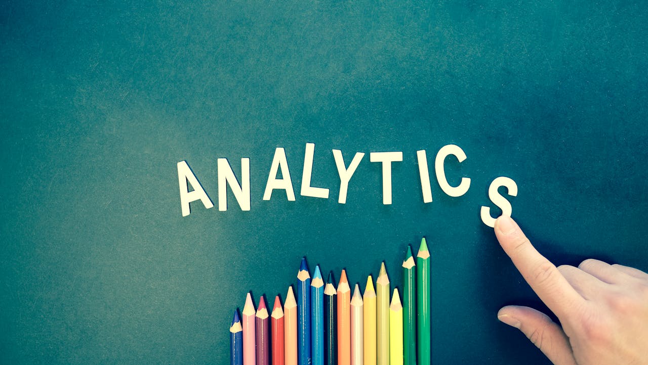 embark Colored pencils and letters spelling ANALYTICS on a textured background with a hand.